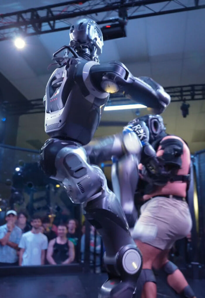 Robot delivering a kick to human opponent in a cage fight