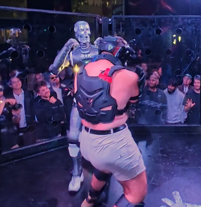 Man in protective gear dodging punch from robot during man vs robot cage fight