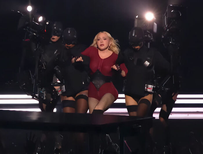 Madonna in red outfit struggling on stage flanked by performers at VMAs Madonna in red outfit struggling on stage flanked by performers at VMAs
