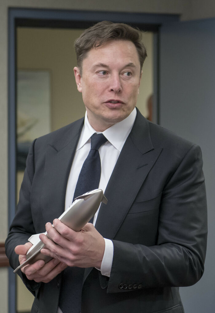 Elon Musk holding a small rocket model, an example of a public figure who could destroy their legacy.