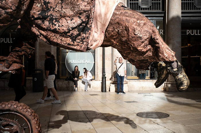 A street photographer captures an odd coincidence: a giant sculpture arm seemingly interacting with a person on a street.