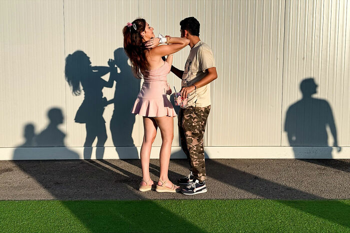A couple posing against a wall, casting long shadows, a coincidental scene captured by a street photographer.