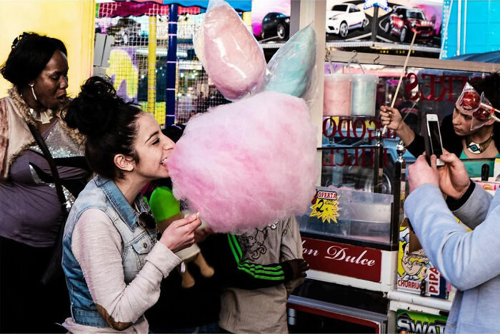 A street photographer captured an odd coincidence: a young woman laughing while eating cotton candy, with other people around.