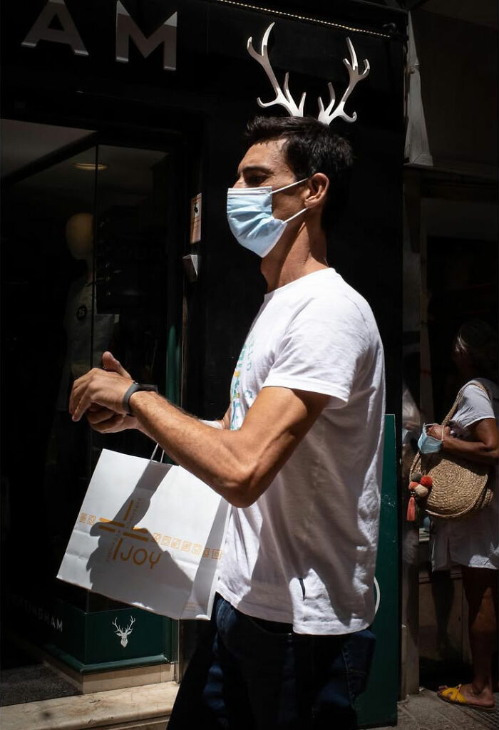 A street photographer captured an odd coincidence: a man wearing a mask and antlers on his head, walking on the street.