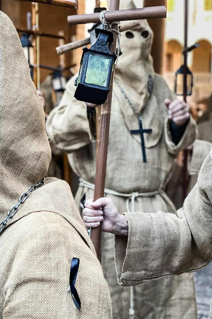 A street photographer captures hooded figures holding a cross and lanterns, an odd and intriguing street scene.
