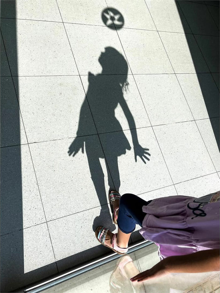 A street photographer captures a girl's shadow playing with a ball, creating an odd coincidence on the pavement.