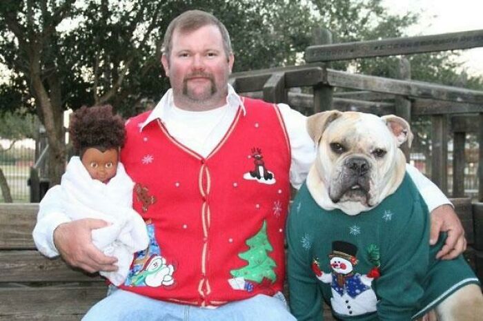 Unhinged image of a man, a doll, and a bulldog wearing matching ugly Christmas sweaters.