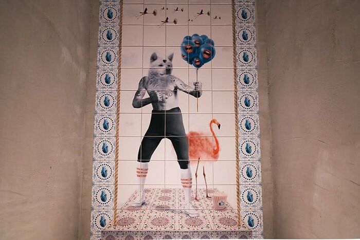 Tile works mural of humanoid dog figure with flamingo and balloon on wall