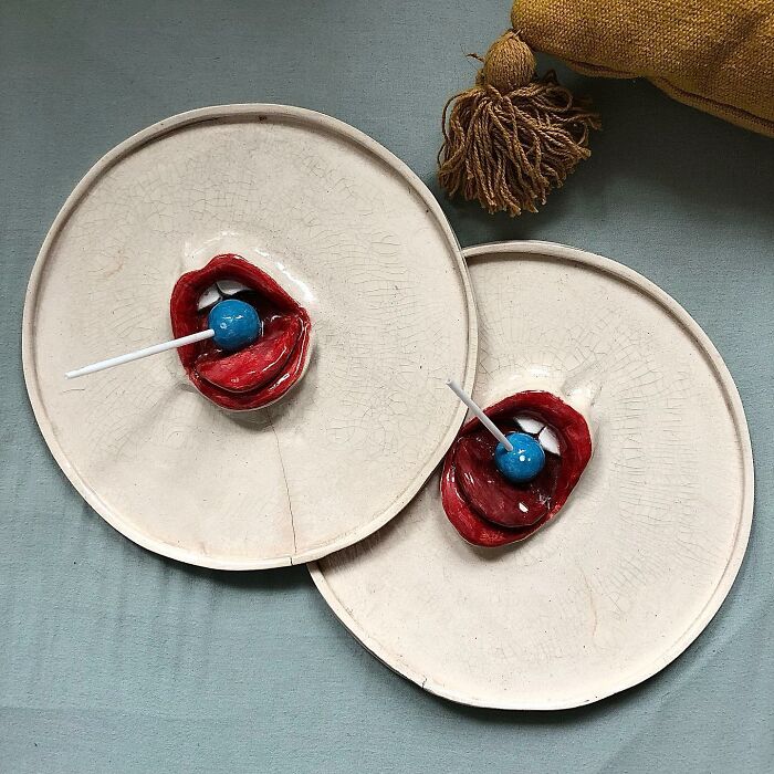Two off-white plates featuring a weird ceramic sculpture of open lips with blue lollipops for home decor.