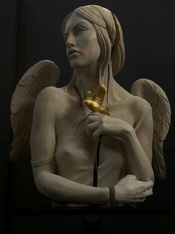 A lifelike sculpture of an angel with a small golden bird, made of wood