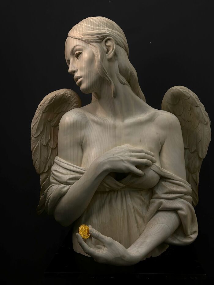 A lifelike sculpture of an angel holding a gold coin, carved from wood