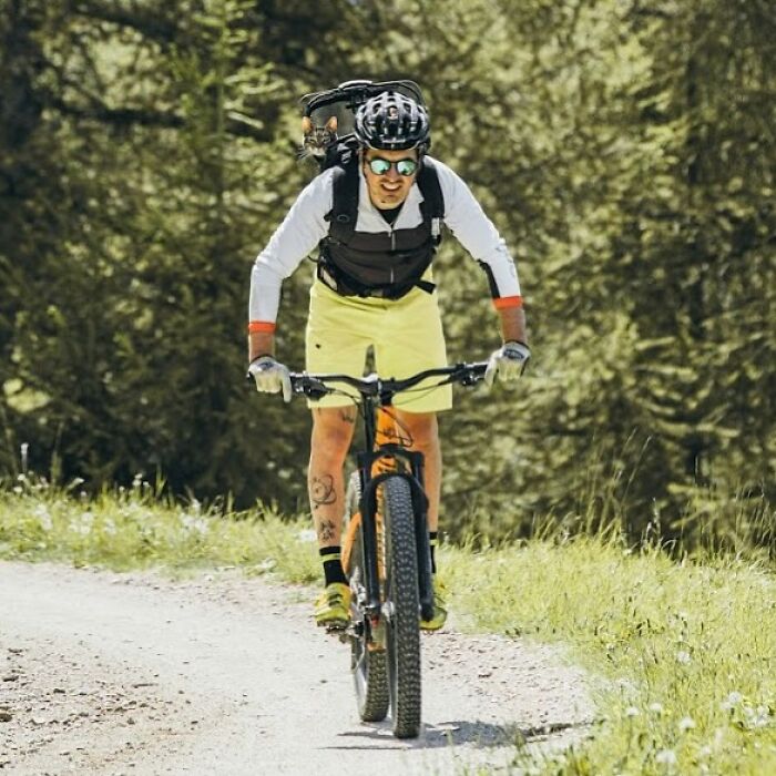 Owner brings cat everywhere for crazy adventures, biking on a dirt path with a cat in a backpack.
