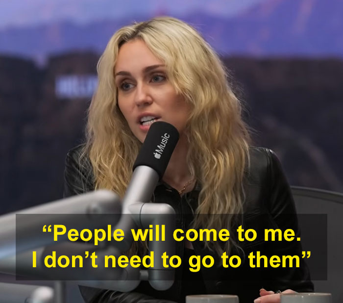 Miley Cyrus speaks into a microphone, making an elitist announcement about fans coming to her.