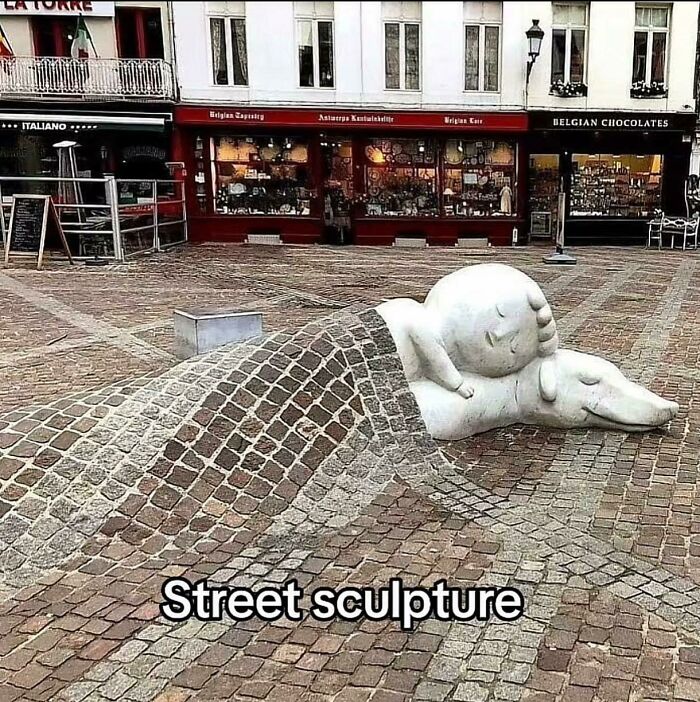 Street sculpture of a sleeping child covered by a cobblestone blanket on a city square