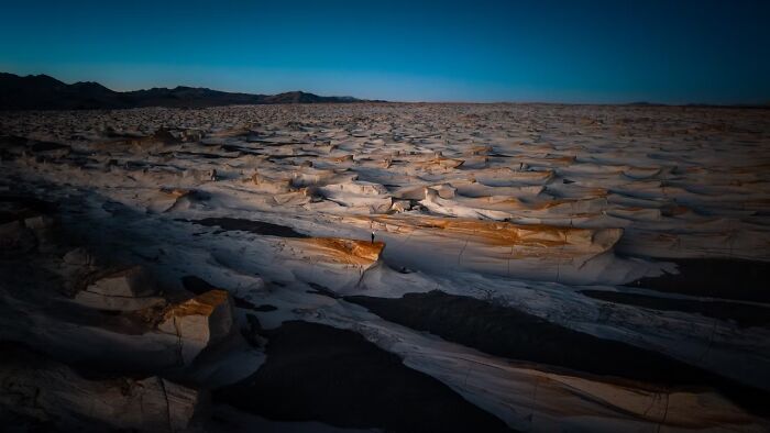 A vast, textured desert landscape under a clear sky, featuring remarkable places and people.