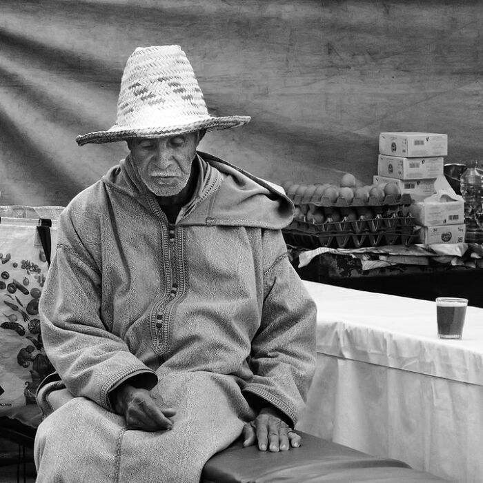 Remarkable travel photos of an older man in traditional attire and straw hat, sitting in a market setting.