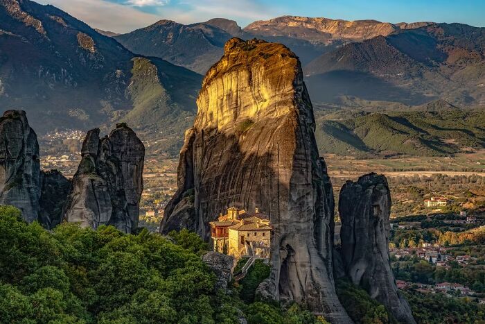 A stunning travel photo of a monastery perched on a towering rock formation amidst mountains, capturing remarkable places.
