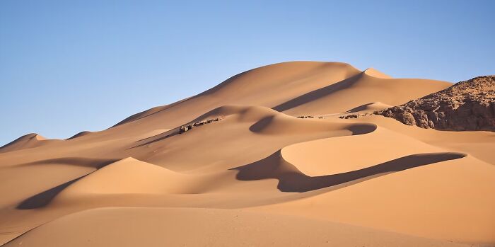 A landscape of vast sand dunes under a clear blue sky, a remarkable place captured in travel photos.