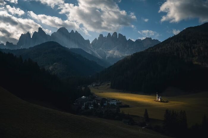 A small village church bathed in sunlight amidst dark mountains, a remarkable place in travel photos.
