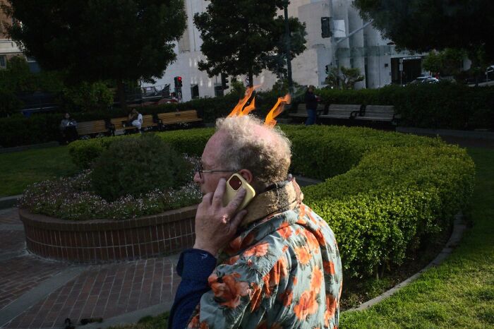 A man with fire-like hair talks on a phone in a park, capturing a candid moment for the URBAN Photo Awards.
