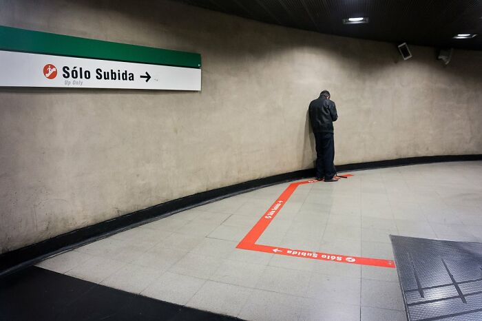 A man leans against a wall in a subway station with an Up Only sign, a candid street photo for URBAN Photo Awards.