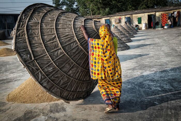 A woman in a colorful sari working with a large straw structure, captured for URBAN Photo Awards.