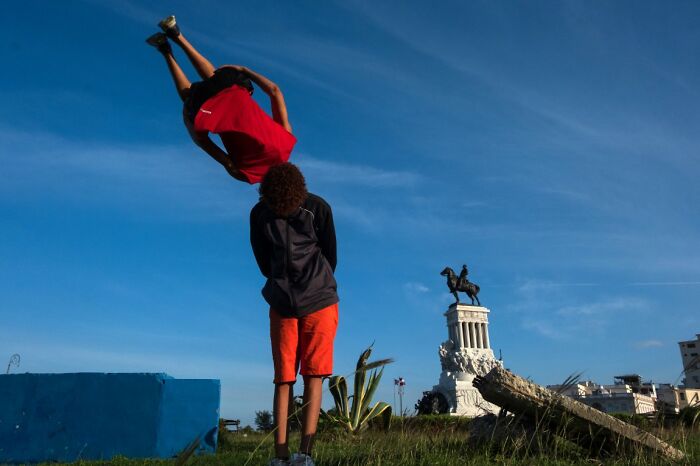 A person doing a backflip in front of a distant statue, an energetic shot for URBAN Photo Awards.