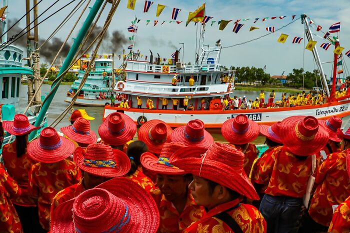 A vibrant street scene capturing a river procession with boats and people in red hats for the URBAN Photo Awards.