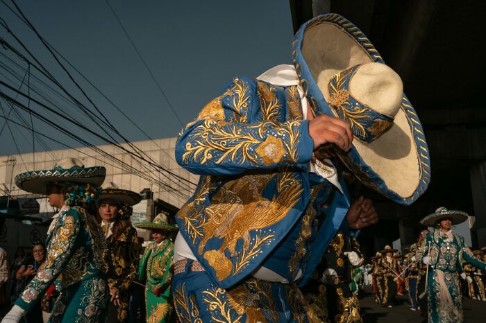 A person in an ornate blue and gold mariachi suit and hat, dancing outdoors, featured in URBAN Photo Awards.