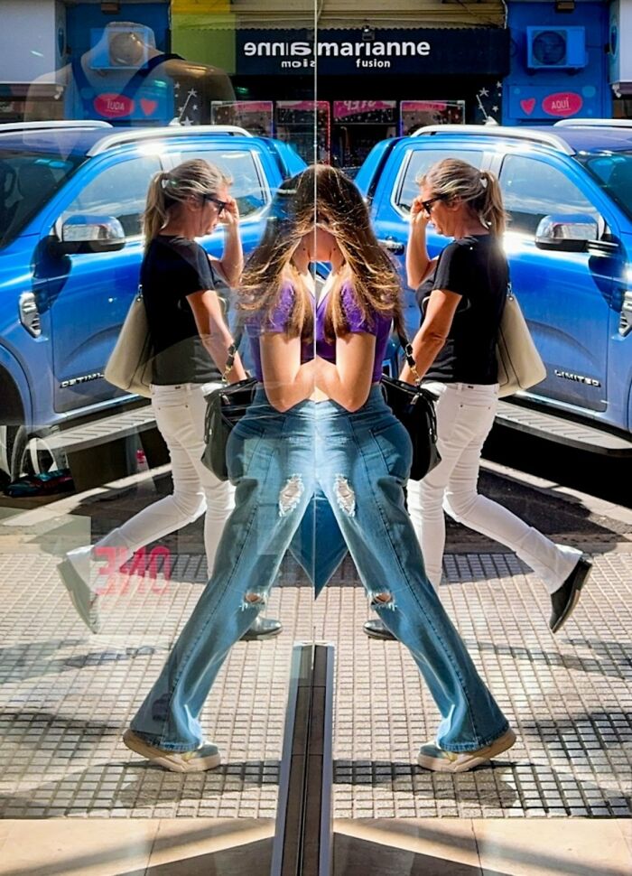 Reflected image of a woman and a blue car on a storefront, a creative street photo for URBAN Photo Awards.