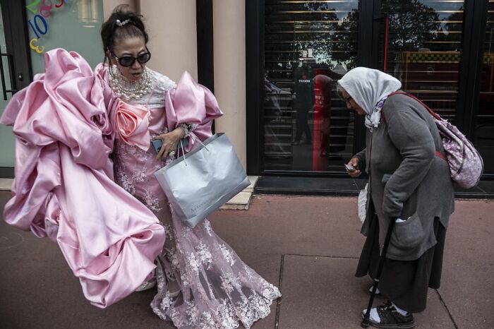 Two women, one in an elaborate pink dress, interact on the street in a candid street photo from the URBAN Photo Awards.