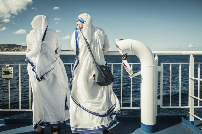 A candid street photo featuring two women in white habits looking out at the sea from a boat for the URBAN Photo Awards.
