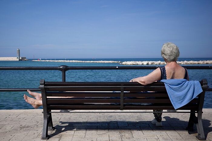 A candid street photo of a woman with her feet up on a bench, looking at the sea for the URBAN Photo Awards.