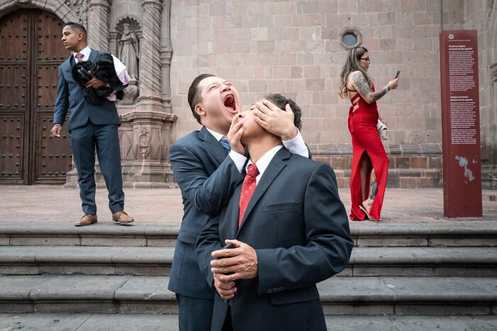 Candid street photo of men in suits, one with a hand over another's eyes, outside a building for the URBAN Photo Awards.