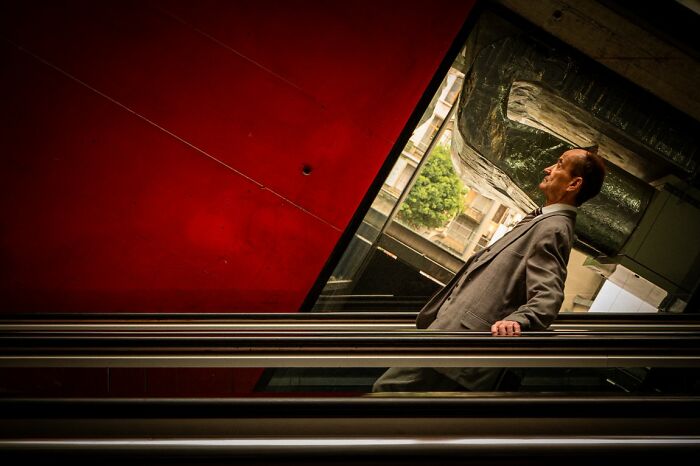 Candid street photo of a man in a suit on an escalator, looking up, with modern architecture for the URBAN Photo Awards.