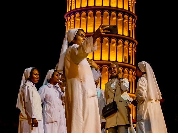 Candid street photo of nuns taking a selfie in front of an illuminated building at night for the URBAN Photo Awards.