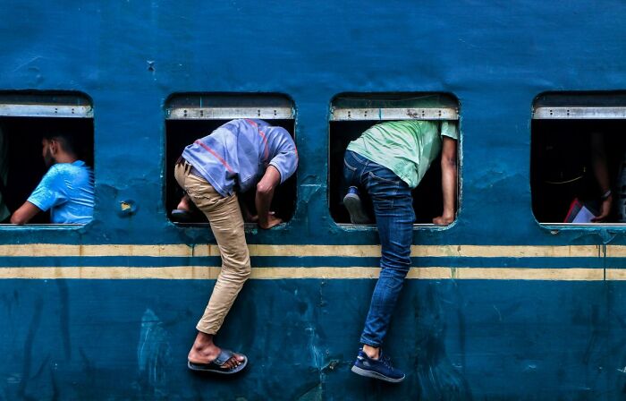 Two people climbing into a blue train window, a candid street photo for URBAN Photo Awards.