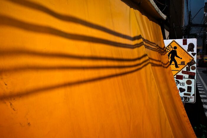 An orange wall with dark shadows and a pedestrian crossing sign, a candid street photo for URBAN Photo Awards.