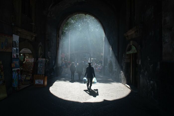 A candid street photo showing a person walking through a sunlit archway, a highlight from the URBAN Photo Awards.
