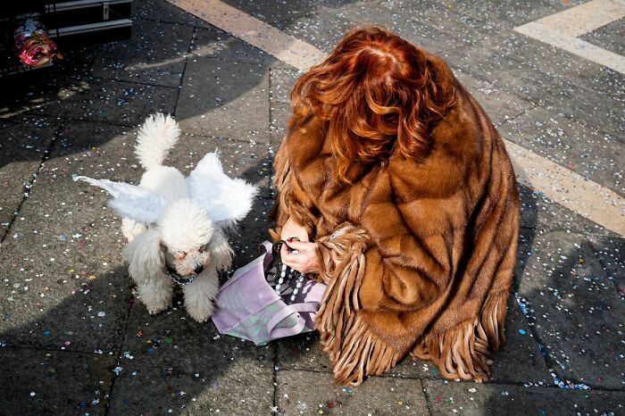 A candid street photo depicting a woman with a fur shawl and a dog with wings, featured in the URBAN Photo Awards.