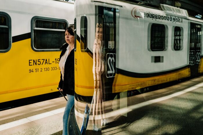A candid street photo capturing a woman walking past a train, with reflections creating an artistic double exposure for URBAN Photo Awards.