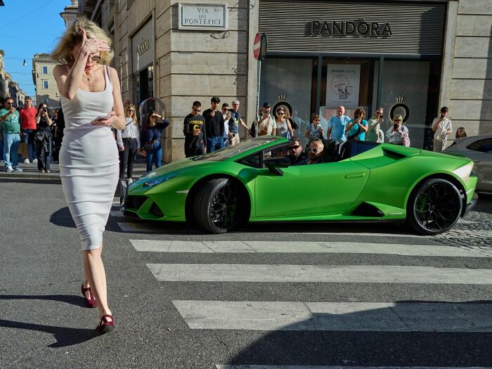 A candid street photo of a woman crossing a street in front of a green Lamborghini, highlighting URBAN Photo Awards.