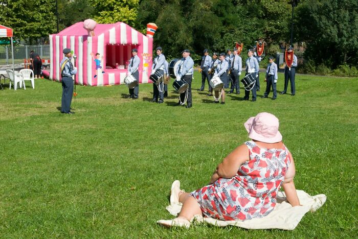 Candid street photo of a person sitting on grass, watching a band perform outdoors at an URBAN event.