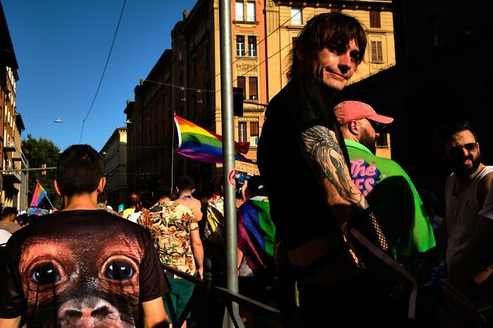 Candid street photo of a man smiling during an URBAN event, with a rainbow flag in the background.