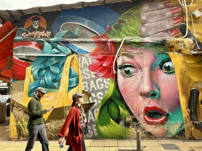 Two people walking past a vibrant street art mural, capturing a dynamic candid street photo for URBAN Photo Awards.