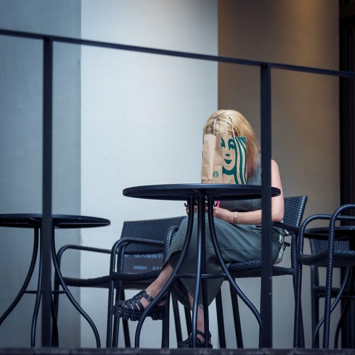 Candid street photo of a woman with a paper bag over her head at an outdoor cafe, an URBAN photo awards entry.