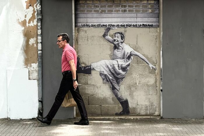 Candid street photo of a man walking past a wall mural of a person kicking, an URBAN photo awards entry.