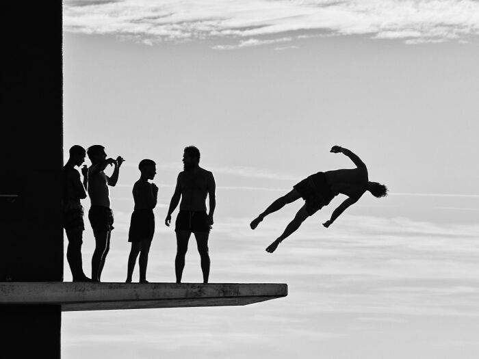 Silhouetted figures on a diving board, with one person mid-air in a dive, a dramatic image for URBAN Photo Awards.
