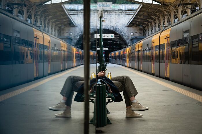 Candid Street Photos of a person reflected upside down on a bench at a train station platform, URBAN Photo Awards.