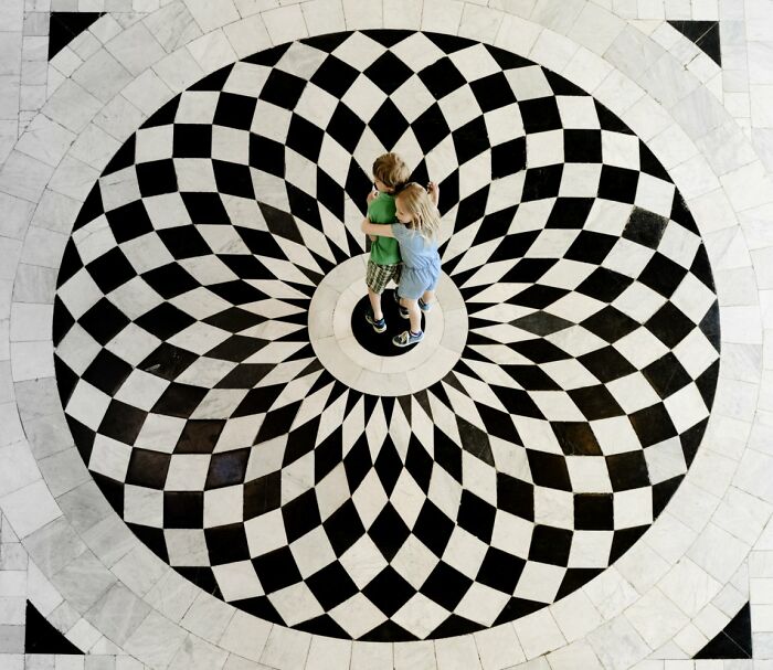 Candid Street Photos of two children hugging on a black and white checkerboard floor, URBAN Photo Awards.